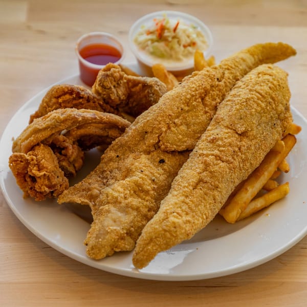Crispy fried fish fillets, chicken wings, french fries, coleslaw, and sweet chili sauce on a white plate.