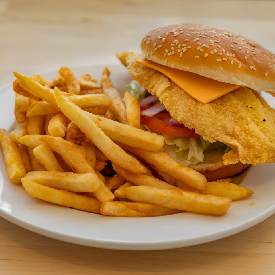 A fried fish sandwich with cheese, lettuce, tomato, and onion, served with a side of fries.