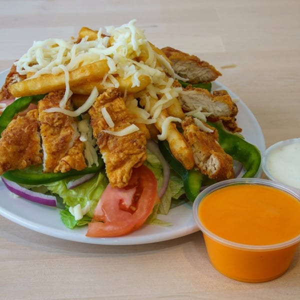 Crispy fried chicken pieces, french fries, shredded cheese, and fresh vegetables on a white plate.