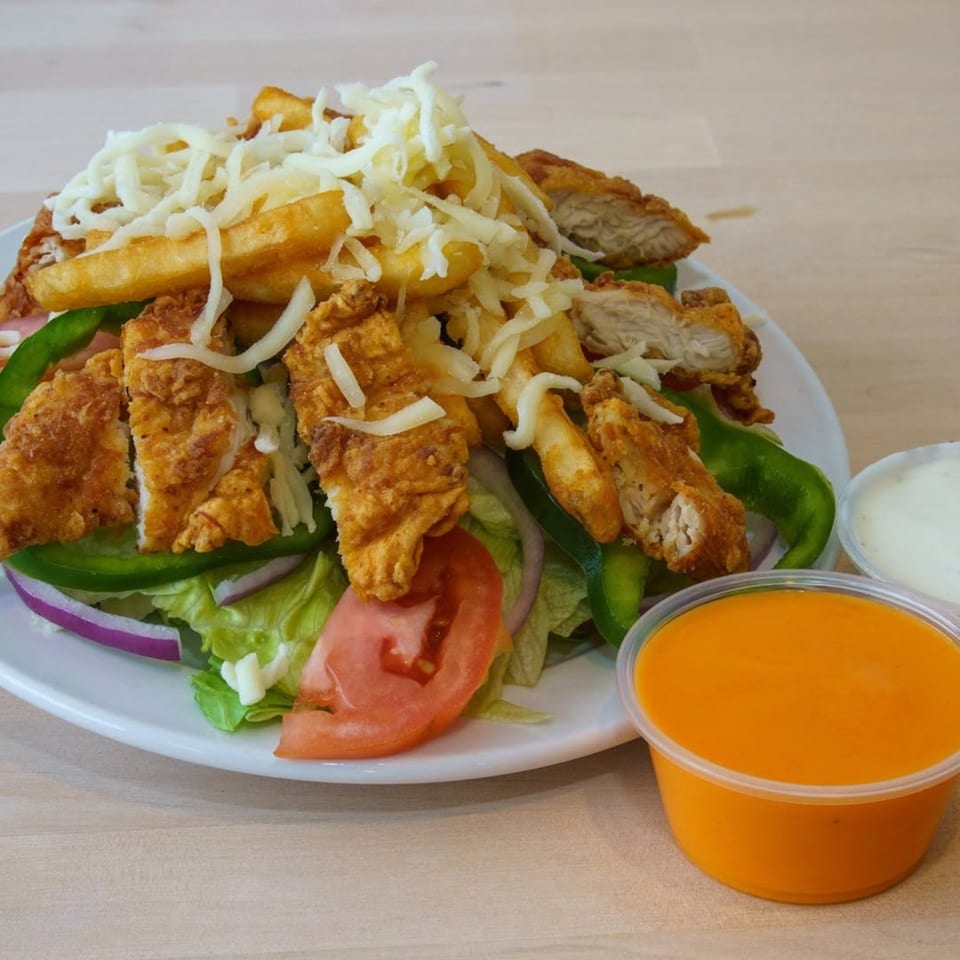 Crispy fried chicken pieces, french fries, shredded cheese, and fresh vegetables on a white plate.