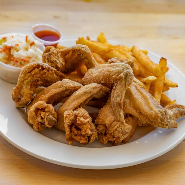 A plate of crispy fried chicken wings, golden french fries, coleslaw, and dipping sauce.